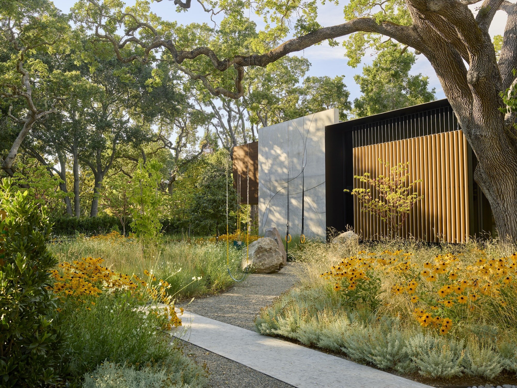 Native prairie planting with black-eyed Susans, mature oaks, and a modern wood-screen pavilion